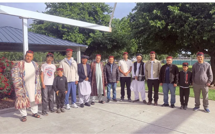Community members of all ages standing together in traditional embroidered caps